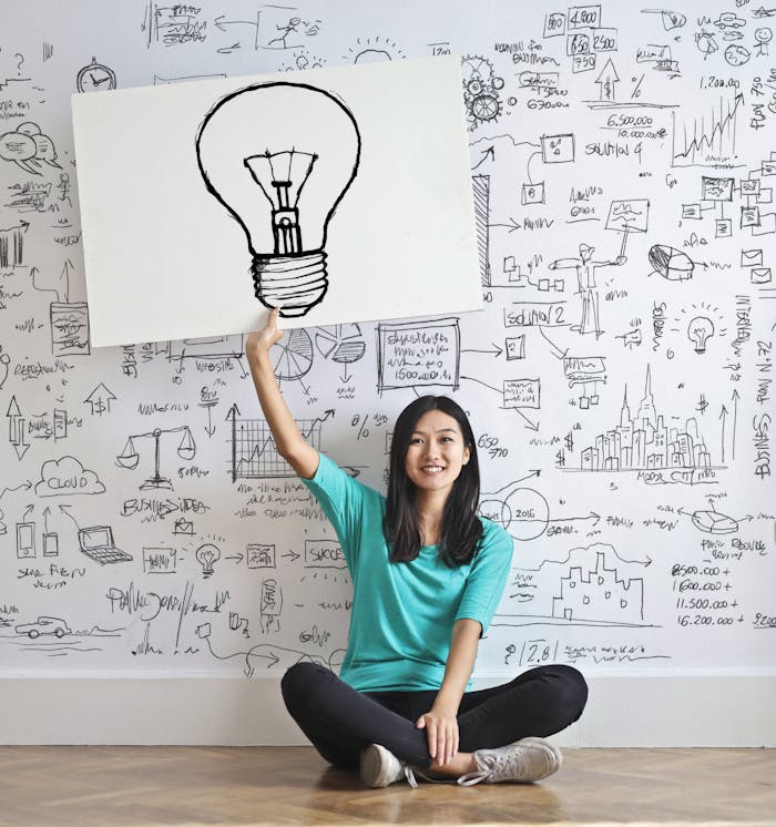 who-we-are Young woman holds a light bulb drawing against a creative brainstorming wall.